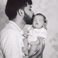 A tender black and white moment of a father kissing his sleeping newborn's forehead. This classic portrait is full of love and peaceful emotion.