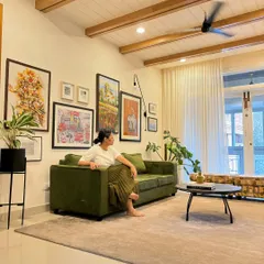 Here I am in a recently completed living room, enjoying the final result. The design features a vaulted ceiling with wooden beams, a curated gallery wall, and an olive green sofa to create a space that is personal, artistic, and full of character.
