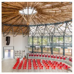 An interior view of the Koodaaram Pavilion in Kochi, a performance space designed for the Kochi-Muziris Biennale. The intricate bamboo canopy and steel structure create a space that is both grand and light, with tiered seating that fosters a sense of community among the audience.