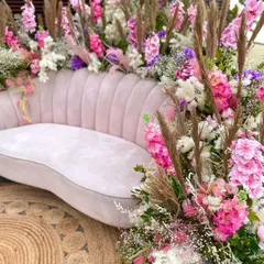 A luxurious seating option for a bride or for a photo booth. This plush pink sofa is surrounded by an explosion of colorful flowers and pampas grass, creating a very high-end look.