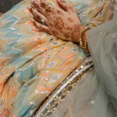 A detail shot showcasing texture and tradition. The intricate gota patti work on the bride's pastel lehenga is perfectly complemented by the delicate patterns of her bridal henna.