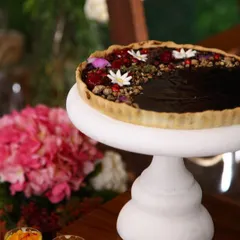A beautiful chocolate tart on a white pedestal, adorned with fresh berries and edible flowers. We pride ourselves on creating desserts that are innovative, flavourful, and visually indulgent.
