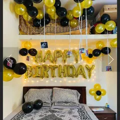 A simple and classic birthday bedroom surprise. The setup includes 'Happy Birthday' foil letters, balloons on the ceiling with hanging photos, and a color theme of black and gold.
