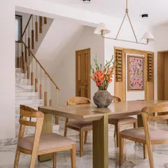 The dining area in Cocoon House is bright and welcoming, set against a backdrop of white marble floors and clean lines. We designed the space with a light wood dining set and a modern chandelier, while a traditional Phulkari artwork adds a touch of color and cultural heritage.
