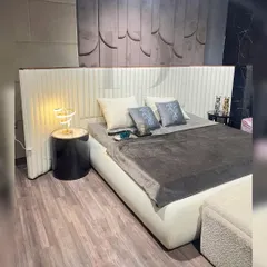 This bedroom exudes modern elegance with a wingback, channel-tufted headboard in off-white fabric. The bed is set against a textured wall panel, creating a sophisticated, layered look.