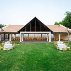 The main hall of the Samavana wedding venue opens onto a large, manicured lawn, creating a flexible space for large gatherings. The high, pitched roof and open sides allow for an airy, pavilion-like feel that connects the celebration to the outdoors.