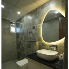 This bathroom at Saya Gold uses textured grey tiles and a uniquely shaped backlit mirror to create a modern and moody atmosphere. The vessel sink sits atop a black marble counter for a touch of luxury.