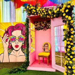 This fun photo booth was designed for a Mehandi party. It features a pink telephone booth structure adorned with yellow and white flowers, set against a pop art backdrop, creating a unique and interactive spot for guests.