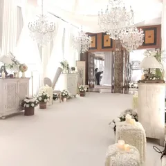 An all-white themed entrance passage for a sophisticated reception. The decor features vintage-style furniture, abundant white florals, and sparkling chandeliers, creating a dreamy and elegant welcome.