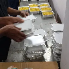 Our staff carefully lidding the packed meal containers. We maintain the highest standards of hygiene throughout the packing process.