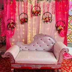 A simple and elegant stage decor with a pink curtain backdrop and hanging floral hoops, perfect for an engagement or naming ceremony.