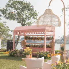 A pastel pink cabana stands by the water at our 'Riverside Brunch', surrounded by yellow flowers and featuring a stylish wicker floor lamp.