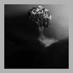 An artistic, moody portrait captured with a slow shutter speed to create a sense of motion. The model wears a floral headpiece, and the black and white treatment emphasizes the ethereal, dreamlike quality of the image.