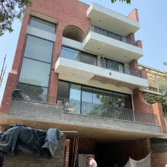 Another view of the Waterfall house under construction, highlighting its volumetric design with cantilevered balconies and double-height window openings. The raw concrete and brick structure shows the building's modern form.