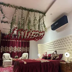 This stunning setup features a ceiling adorned with hanging floral strings and a floating cloud of red roses over the bed, set against rich, dark curtains for a dramatic effect.