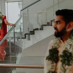 A "first look" style shot on a modern staircase, capturing the groom's reaction as he sees his bride in her stunning South Indian wedding attire.