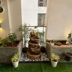 A multi-tiered cascading water fountain adds gentle sound and movement to this balcony garden. Placed on a bed of white pebbles and surrounded by papyrus plants, it creates a naturalistic and calming corner.