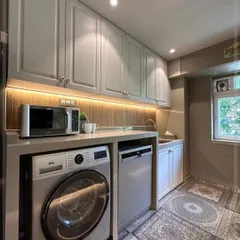 This shot highlights the utility side of the kitchen, where we have seamlessly integrated the washing machine and dishwasher under the counter. The overhead cabinets in a light grey membrane finish provide ample storage.