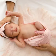 Held safely in their parents' hands, this sleeping baby girl is a picture of serenity. The soft pink wrap and headband add a delicate touch to this newborn portrait.