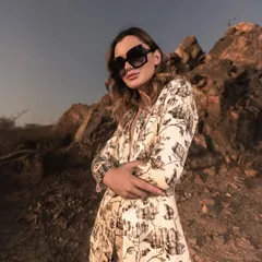 A close-up shot using the natural landscape and a low angle to create a powerful, confident pose. The lighting highlights the model's expression and the texture of the printed blazer.