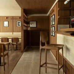 The coffee bar at QBF Coffee, showcasing a harmonious blend of materials. The travertine stone front, wood paneling, and minimalist bar stools reflect a design philosophy rooted in simplicity, warmth, and tactile honesty.