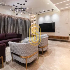 A different perspective of the living room, highlighting the quilted grey armchairs with gold-finished frames. This view shows the relationship between the seating arrangement and the custom TV wall unit.