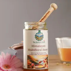 A styled shot of The Himalayan Farms multifloral honey, with a wooden dipper and flowers to create a natural, wholesome feel. The lighting highlights the honey's golden color and texture.