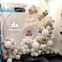 A sophisticated balloon decoration for an office party to celebrate a boss's birthday. The setup includes a silver ring frame, a stylish garland of white, grey, and taupe balloons, and a 'Big Boss' sign.