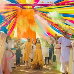 The joy of a Haldi ceremony captured perfectly. The couple celebrates amidst a shower of colorful smoke bombs under a vibrant canopy of drapes, showing how decor can enhance the experience.