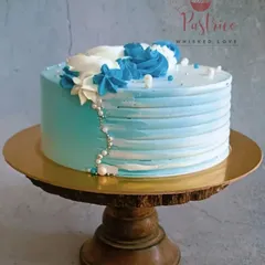 The same blue floral cake, shown from a different angle on a rustic wooden stand. This view highlights the height of the cake and the cascading pearl details.