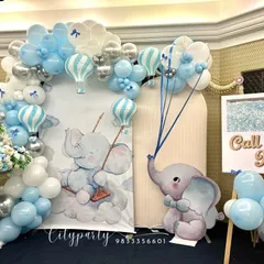 A beautiful naming ceremony decoration with a baby elephant and hot air balloon theme. The setup includes a custom backdrop, a blue, white, and silver balloon arch, and an easel for the name reveal.