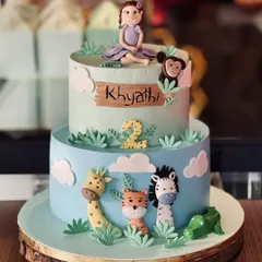 A two-tier jungle theme cake for Khyathi's second birthday. This fondant cake features hand-crafted animal figures like a giraffe, tiger, and monkey, making it a delightful centerpiece.