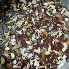 This is the top of my dry fruit brownie slab before it gets cut. It's generously topped with a mix of sliced almonds and pistachios, adding a wonderful crunch and nutty flavor to the rich chocolate.