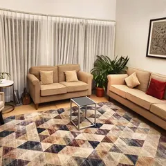 In this South Delhi bungalow with tall ceilings and original terrazzo floors, we introduced color and texture with a geometric rug. The neutral furniture palette allows the rug and the large traditional artwork to become the focal points, creating a cozy yet modern drawing room.