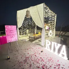 An elegant bachelorette party on a rooftop, complete with a draped canopy, fairy light curtains, personalized marquee letters, and scattered rose petals for a luxurious feel.
