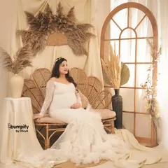 A beautiful, light-filled portrait in our boho corner. The mom-to-be is seated on a wicker sofa in a lovely white lace gown, surrounded by pampas grass and soft fabrics.