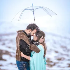An intimate and emotional portrait of a couple embracing under an umbrella during a snowfall in Kashmir. This shot perfectly captures the cozy feeling of being in love against a vast, cold landscape.
