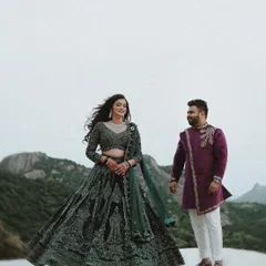 The couple stands against a breathtaking mountain landscape, the bride's intricate lehenga twirling, creating an epic and romantic portrait.