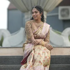 A full length view of the bride seated, showing the flow and richness of her floral silk saree. The custom blouse sparkles, tying the entire traditional look together with a touch of modern craftsmanship.