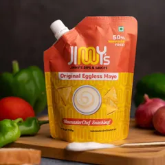 A clean and simple product shot of Jimmy's Eggless Mayonnaise. The pouch is the hero, surrounded by fresh vegetables to suggest its use and versatility in the kitchen.