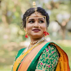 A portrait of a graceful Maharashtrian bride. Her look features a neatly tied bun, traditional gold jewelry, and makeup that highlights her natural elegance against a beautiful outdoor backdrop.