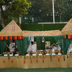 A closer look at our village-themed buffet counter. The setup features bamboo-style huts with colorful tassels and green drapes, creating an authentic, rustic feel that perfectly complements a traditional Indian menu.