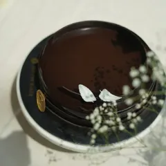 A top-down view of the Belgium Chocolate Cake, adorned with delicate white chocolate leaves and baby's breath. It’s a simple, elegant design that hints at the rich flavor within.