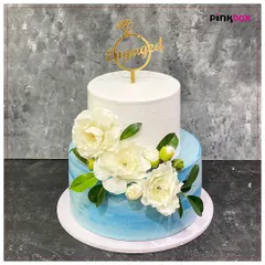 A stunning two-tiered engagement cake with a blue watercolor effect and elegant white sugar flowers. The "Engaged" topper adds the perfect finishing touch to celebrate a new beginning.