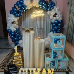 A classic blue and white balloon ring decoration for a boy's birthday, complete with a neon sign, 'B-A-B-Y' blocks, and personalized light-up name.