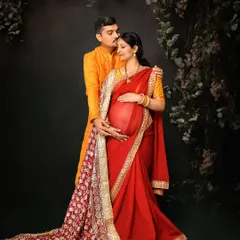 A stunning portrait of an expecting couple in traditional Indian attire. The rich red and gold of the saree and the vibrant yellow of the kurta create a visually splendid and culturally rich image.