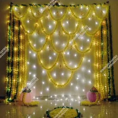 An elegant wall backdrop made of yellow marigold garlands and lit with fairy lights, perfect for any festive occasion at home.