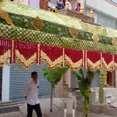Here is a closer look at the craftsmanship involved in a traditional *chappra*. The roof is made of intricately woven leaves, while the front is decorated with beautiful red and white floral hangings, blending natural materials with classic floral art.