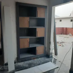 A custom shelving unit for an office reception being assembled. The two-tone design with wood-finish shutters and a dark grey frame is visible even during the construction phase.