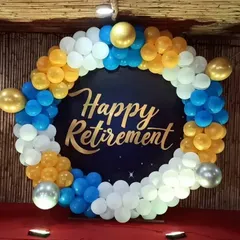 A cheerful setup for a retirement party. I designed a circular backdrop with a 'Happy Retirement' message, framed by a balloon garland in blue, yellow, and white.